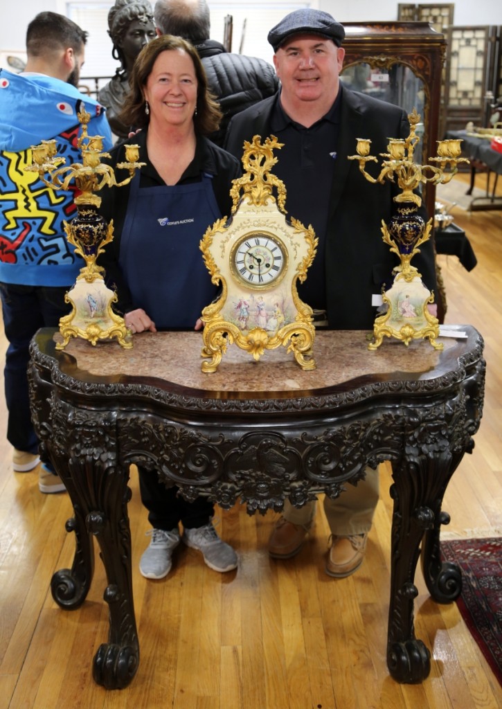 Nancy Wyman, vice president of Coyle’s Auction, stands with president and auctioneer Michael Coyle. In front of them is their top lot, a heavily carved Asian teakwood console with inset marble top that brought $7,820. The three-piece garniture set with clock and candelabra sold for $978.