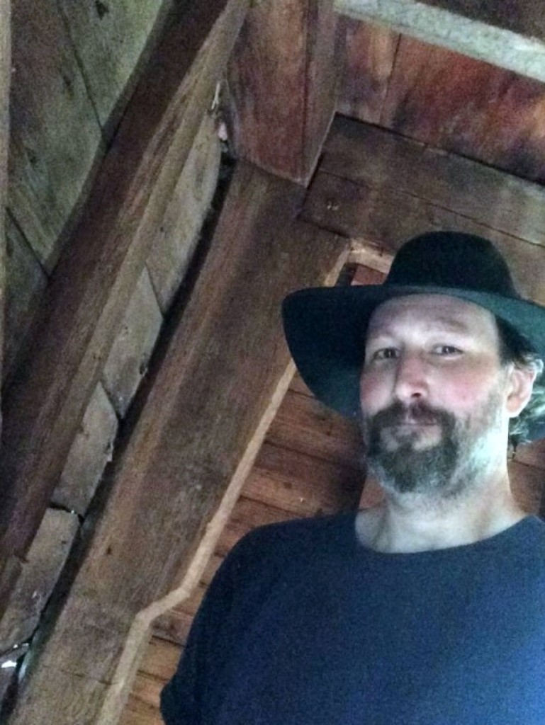 Young standing in the front corner of the house he has disassembled. Behind him is a gunstock or jowel post, suggesting a possible   Seventeenth Century construction date.