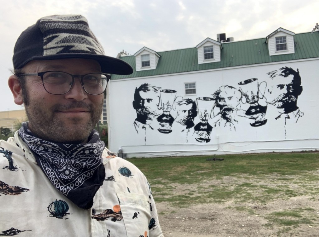 Artist Zach DePolo stands in front of the George Ohr mural.