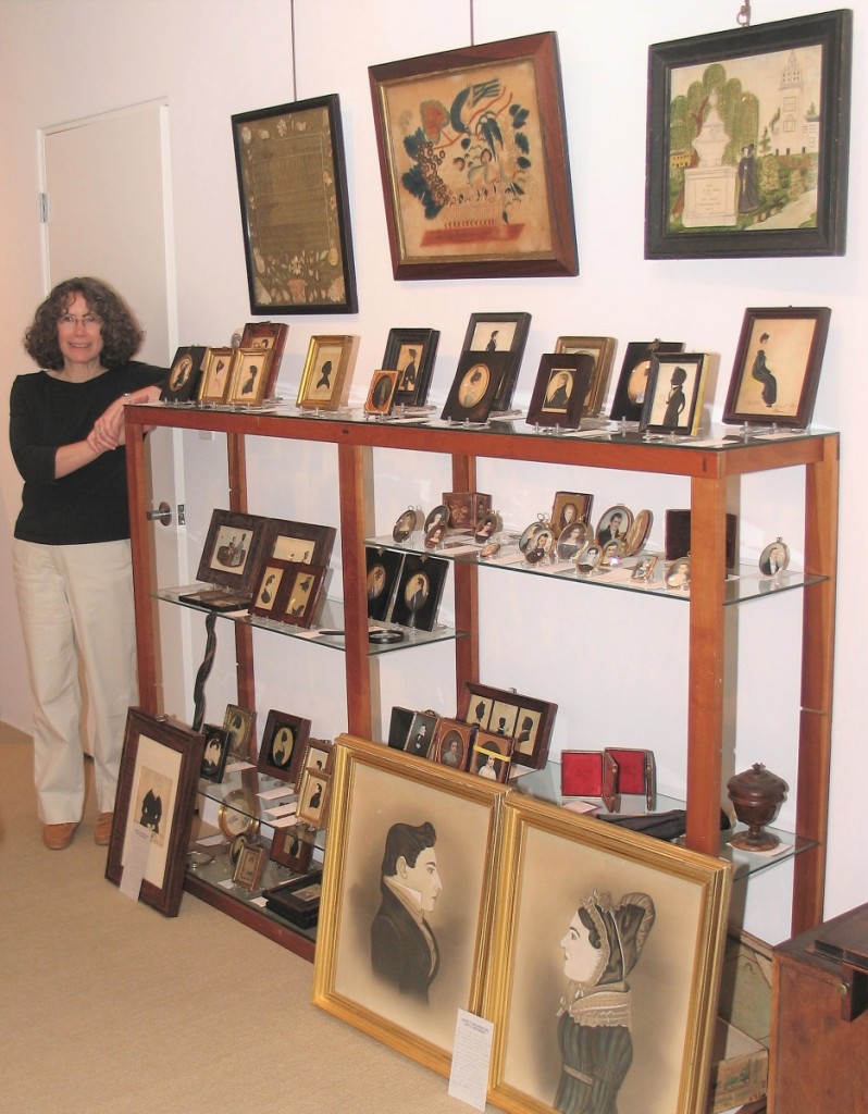 Joan stands next to a collection of small-scale and miniature folk art portraits.