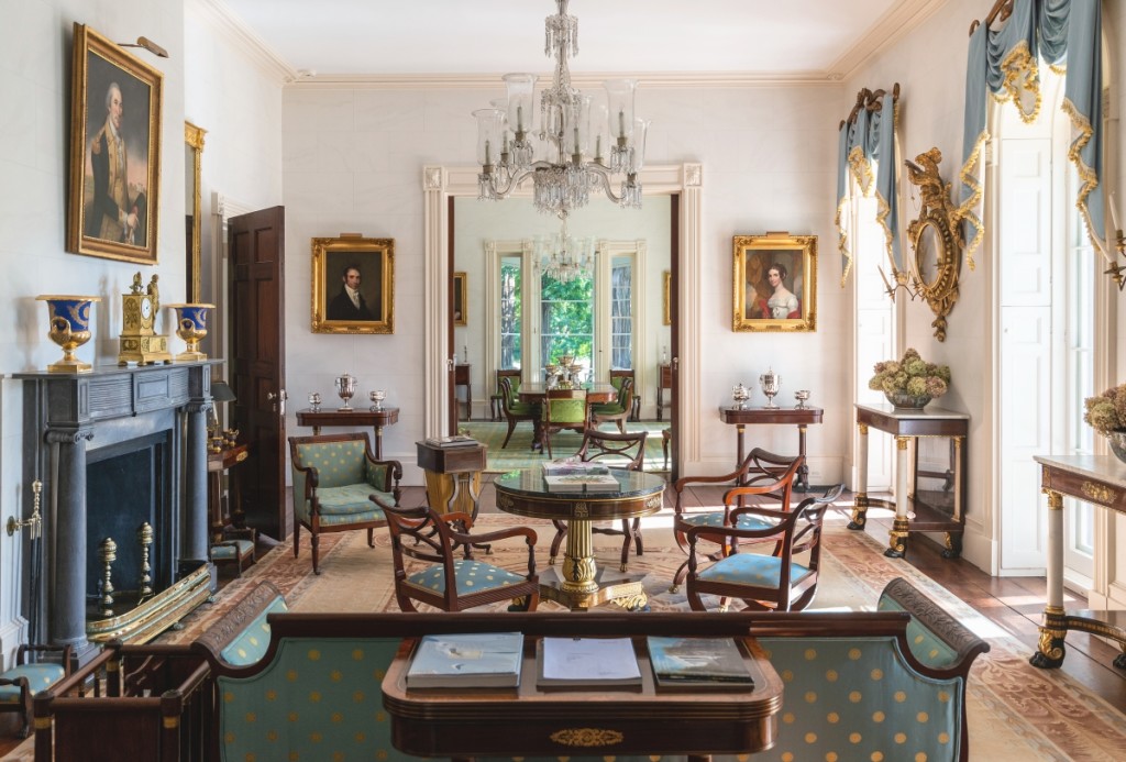The Drawing Room at Edgewater looking toward the Dining Room. The portrait over the mantel is “George Washington Before Nassau Hall” by Charles Peale Polk, completed in 1790. The gilt-bronze mantel clock is by Jean-Baptiste Dubuc.  The center table, game table, sofa and canterbury are all by Duncan Phyfe; the pier tables are attributed to Charles-Honore Lannuier. The three armchairs in the center of the room are by Hagen & Meier. The pair of portraits on the back wall depict Moses and Elizabeth Wheeler, completed in 1823 by Gilbert Stuart.