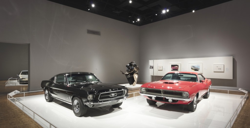 Two classics in a nose-to-nose muscle match-up. At left, the legendary 1967 Ford Mustang Fastback in black — at right, a menacing red 1970 Plymouth Barracuda. The sculpture between them is “Cool Wha Zee,” 1962, by John Chamberlain (1927-2011), who often constructed his works from crushed automobile steel.
