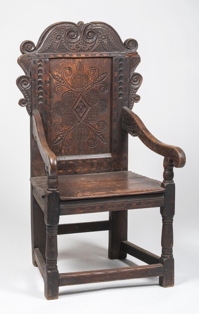 Realizing $3,360 was an English oak Jacobean wainscot armchair with a heavily carved back panel, a two-board plank seat and a box stretcher base.