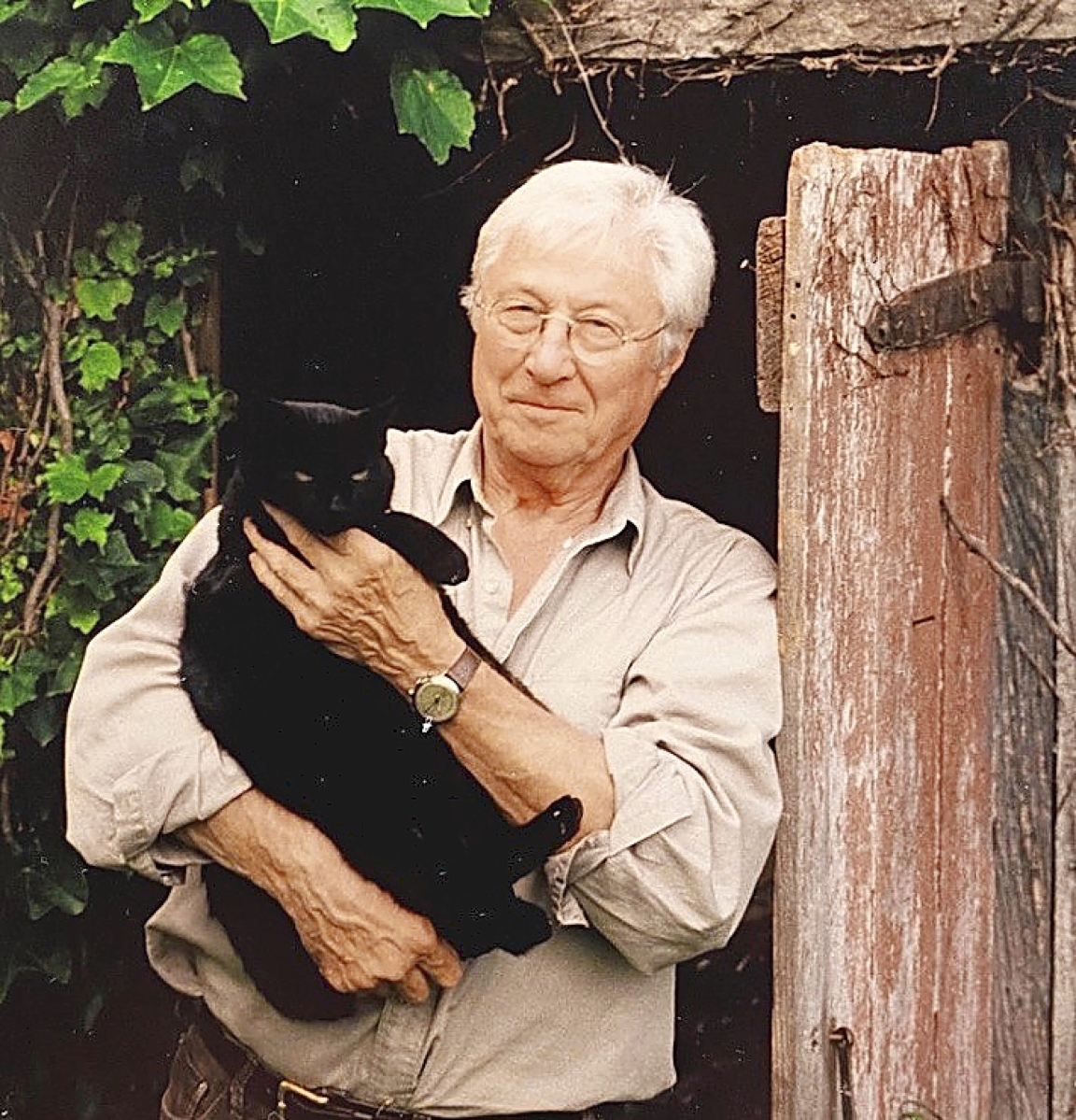 Keno standing with cat “Blackie” in front of the doorway of the Nineteenth Century stone “Smoke house” which still stands today on the Keno property.