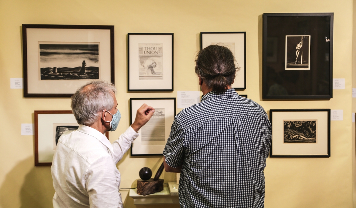 Scott Ferris of J&R Ferris Antiques, left, speaks with a collector about his wall of works by Rockwell Kent. The wood engravings included “Forrest Pool,” circa 1927 and “Man at Mast,” dated 1929. At center are graphite works from a folio produced by Kent as dummies submitted to a publisher for Walt Whitman’s Pioneers, Oh Pioneers. The book was originally titled Thou Union.