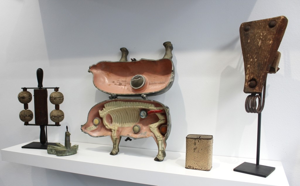 (L-R): Mounted massage rollers and an industrial mold (both with Susan Weschler), a salesman’s sample pig feed model, circa 1924 (Steven Powers), a mounted Nineteenth Century wood and iron bicycle seat (Aarne Anton) and a painted tin bank with aged “alligatored” surface (Janet West).